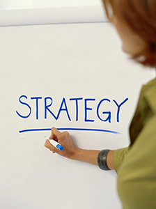A person writing the word strategy on a whiteboard.